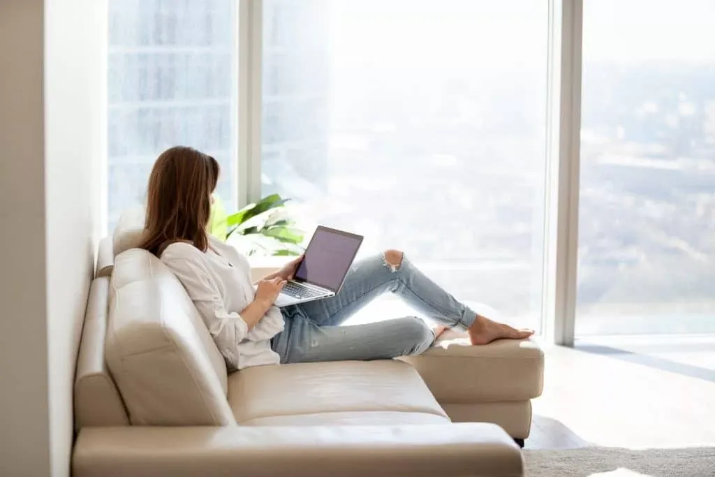 Woman working on her laptop while sitting in a sofa by the window