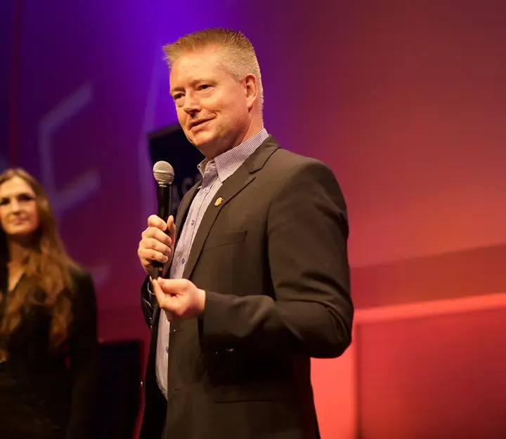 Morten Andersen on stage with a microphone, speaking in front of a converntion audience